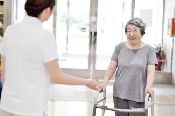 歩行器を使う高齢女性利用者と見守る介護士